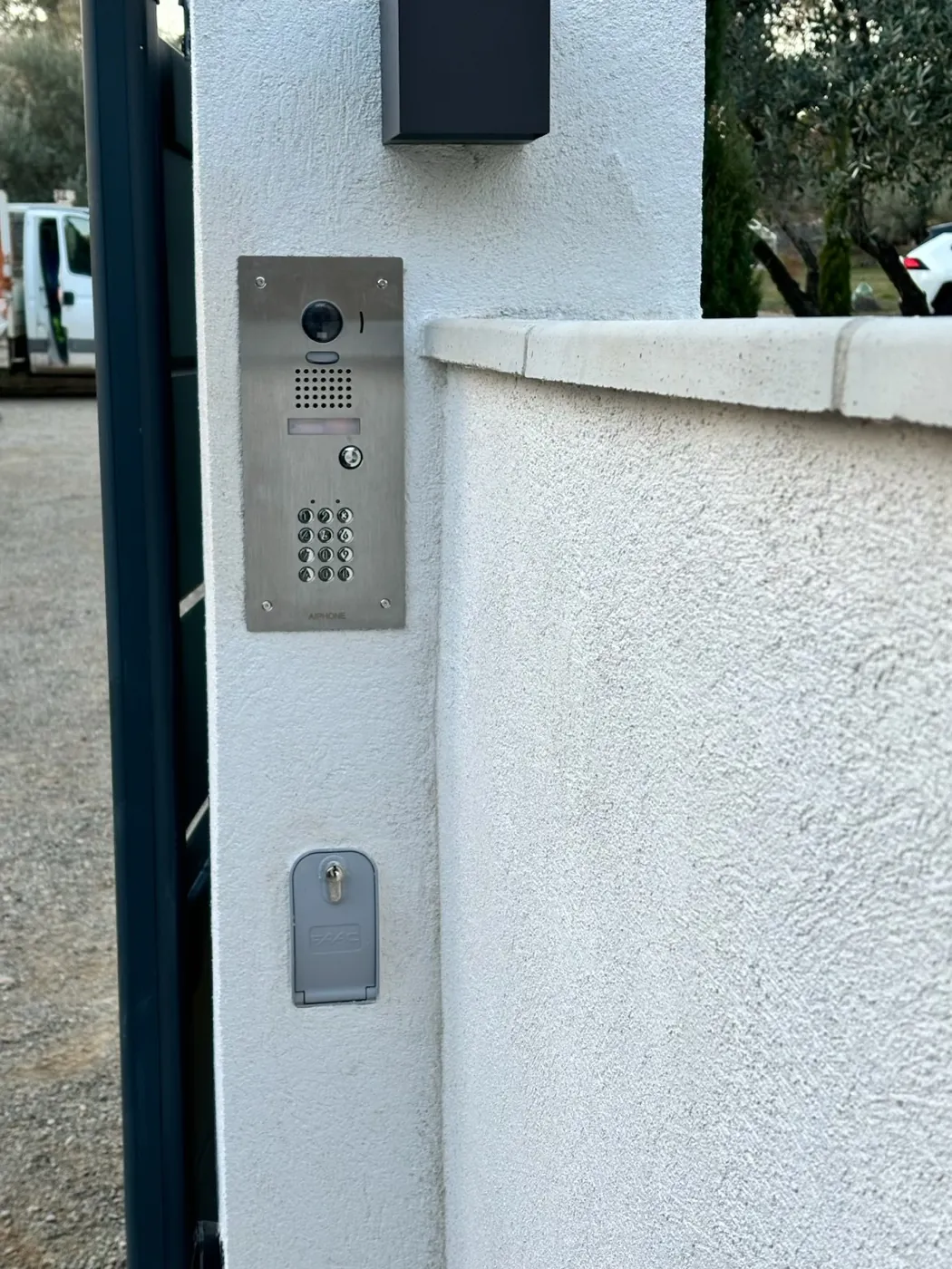 Platine de visiophone Aiphone installée : caméra, haut-parleur, porte-étiquette et clavier à code réunis.