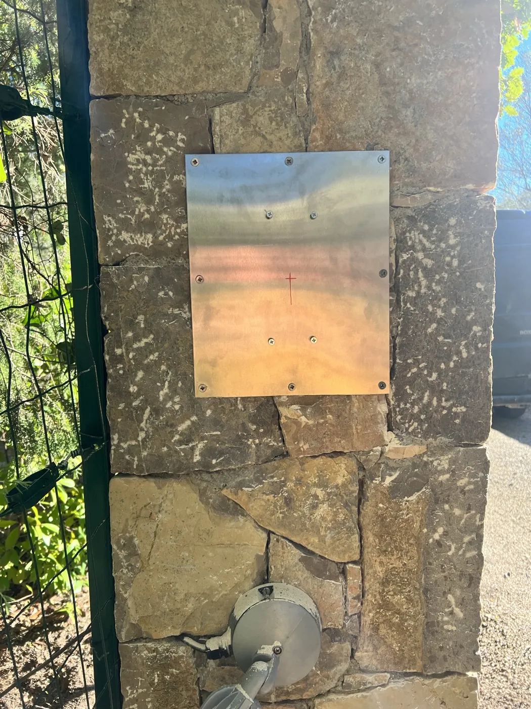 Plaque inox neuve fixée sur le pilier, point de perçage tracé au feutre rouge.