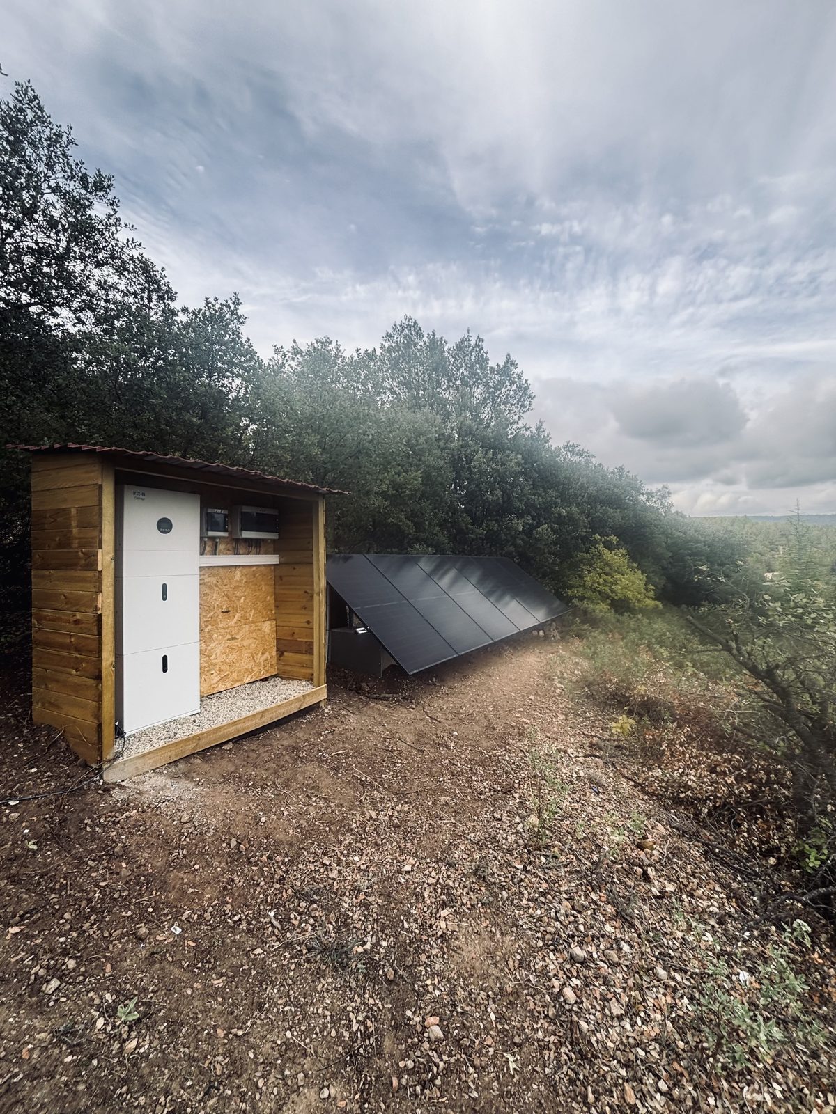 Panneaux au sol et abri technique en bois construit sur place, abritant l'onduleur