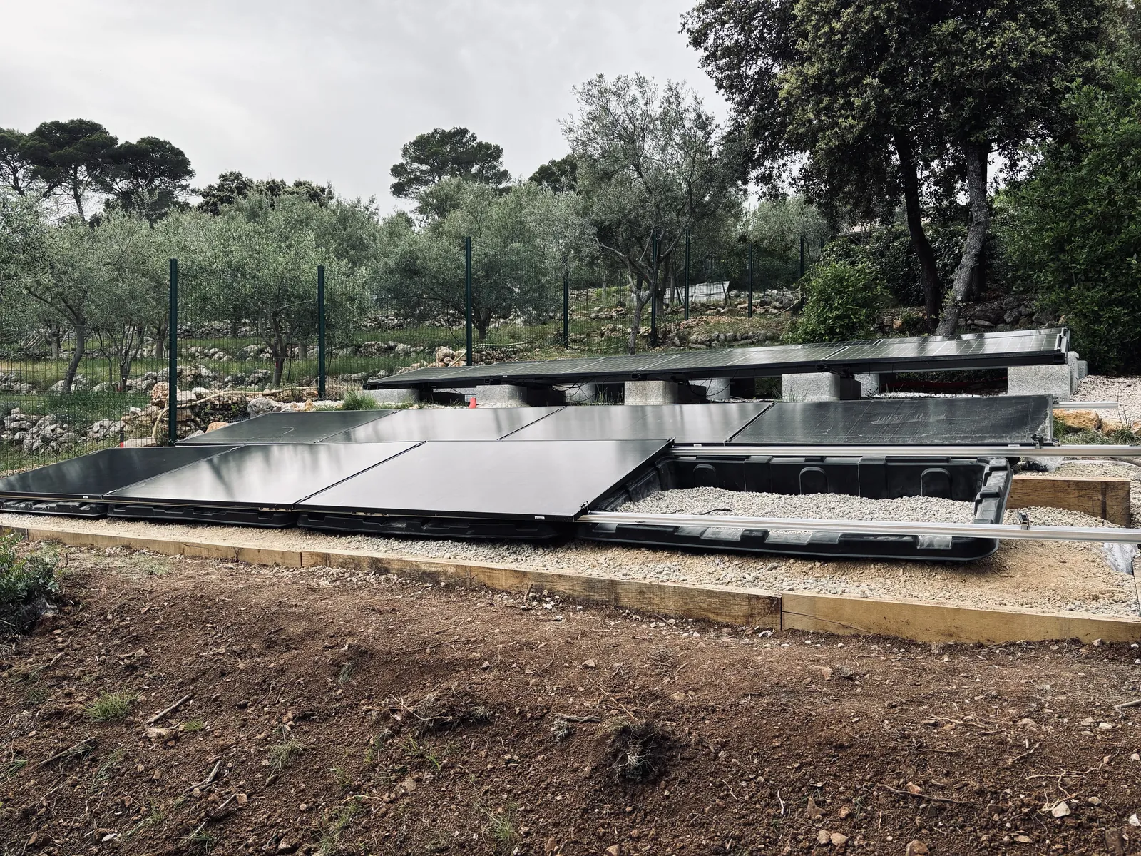Bacs lestés supportant des panneaux solaires, installés entre des oliviers